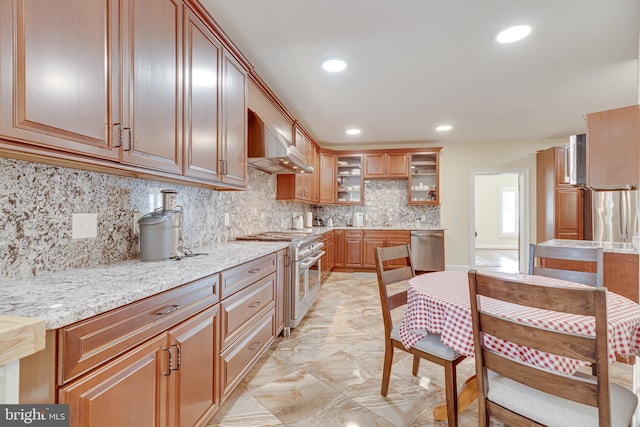 kitchen featuring wall chimney range hood, stainless steel appliances, decorative backsplash, and light stone countertops