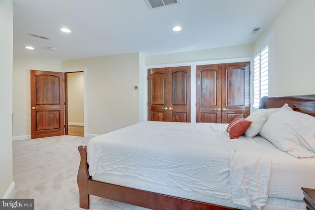 bedroom featuring light colored carpet and multiple closets