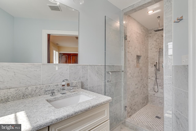 bathroom featuring a shower with door, vanity, and tile walls