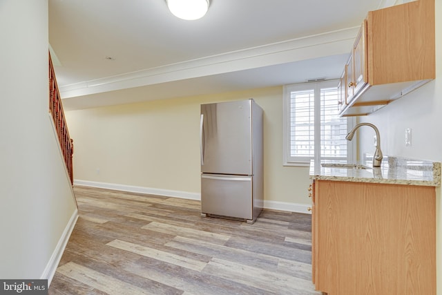 kitchen with light wood-type flooring, stainless steel fridge, sink, and light stone countertops