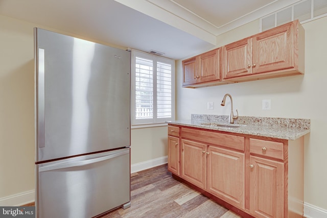 kitchen featuring light brown cabinets, light hardwood / wood-style floors, light stone counters, sink, and stainless steel fridge