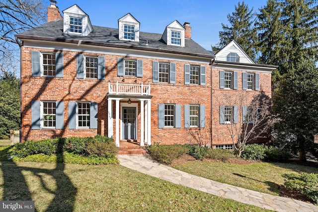 colonial house featuring a front lawn, a chimney, and brick siding