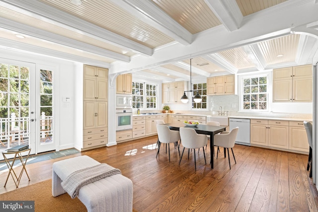 kitchen with a healthy amount of sunlight, white appliances, beam ceiling, and light wood-style floors