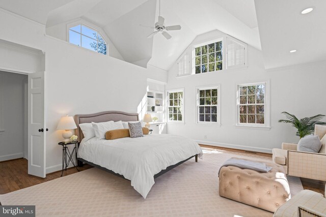 bedroom with high vaulted ceiling, multiple windows, baseboards, and wood finished floors