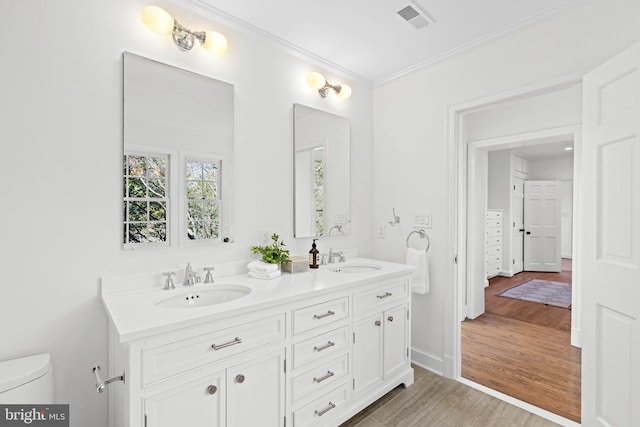 full bath with toilet, wood finished floors, a sink, visible vents, and ornamental molding