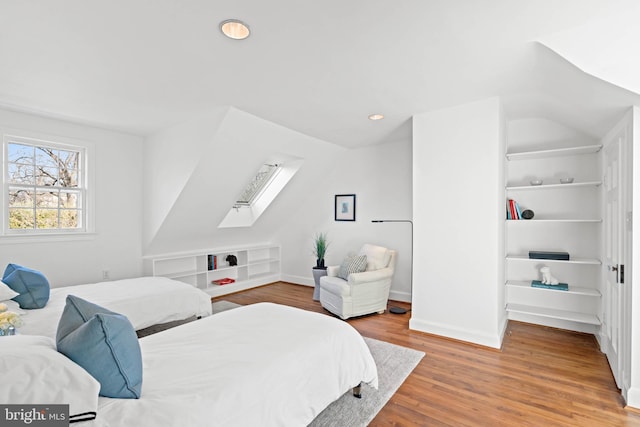 bedroom featuring vaulted ceiling with skylight, baseboards, and wood finished floors