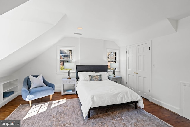 bedroom featuring wood finished floors, visible vents, baseboards, vaulted ceiling, and a closet