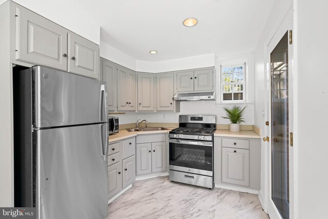 kitchen featuring gray cabinetry, under cabinet range hood, stainless steel appliances, a sink, and marble finish floor