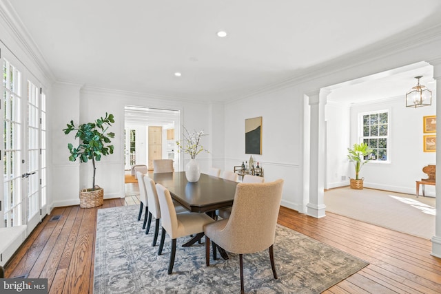 dining room with ornate columns, wood-type flooring, baseboards, and crown molding