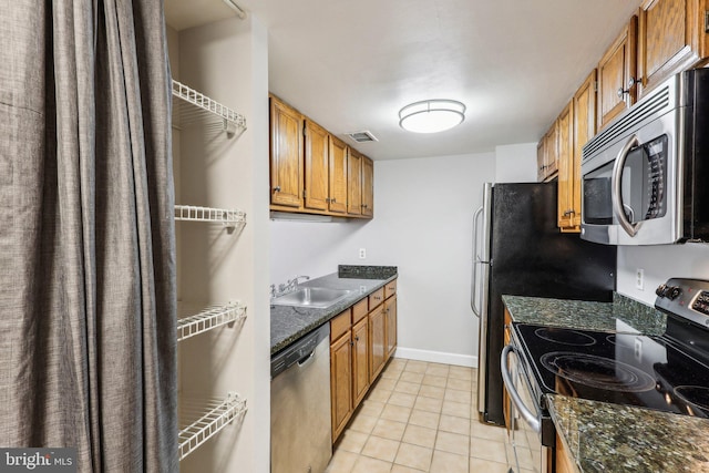 kitchen with sink, dark stone countertops, appliances with stainless steel finishes, and light tile patterned flooring