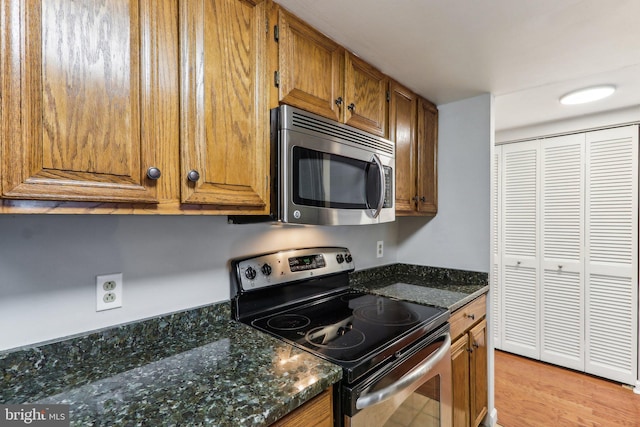 kitchen with light hardwood / wood-style floors, appliances with stainless steel finishes, and dark stone counters