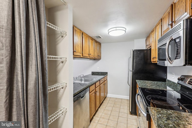 kitchen featuring brown cabinets, stainless steel appliances, a sink, and light tile patterned flooring