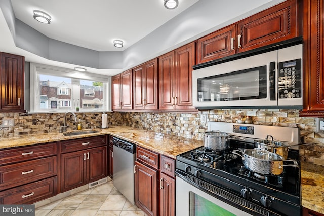 kitchen with tasteful backsplash, light stone countertops, appliances with stainless steel finishes, and sink