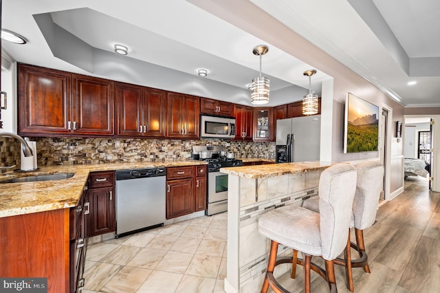 kitchen with pendant lighting, sink, backsplash, light stone counters, and stainless steel appliances