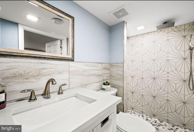 bathroom featuring vanity, a shower, tile walls, and toilet