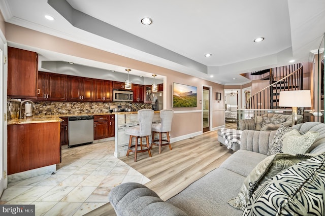 living room with crown molding, sink, light hardwood / wood-style floors, and a tray ceiling