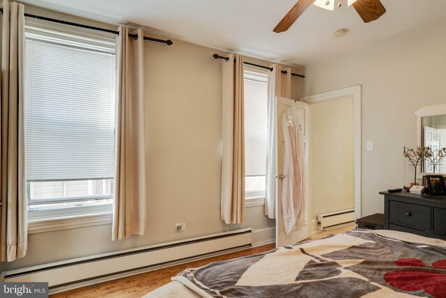 bedroom featuring a baseboard radiator, ceiling fan, light wood-type flooring, and multiple windows