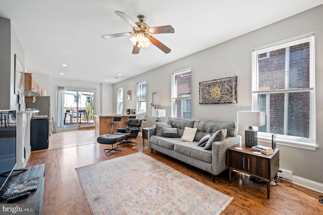 living room with recessed lighting, a baseboard heating unit, wood finished floors, a ceiling fan, and baseboards