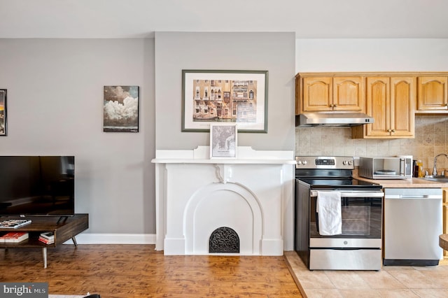 kitchen with backsplash, stainless steel appliances, light countertops, under cabinet range hood, and a sink