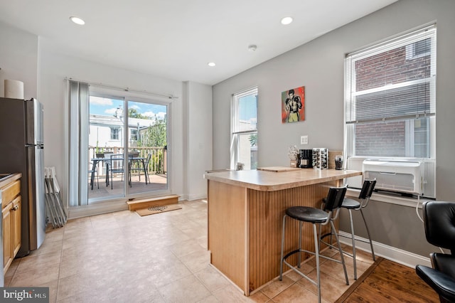 kitchen with a kitchen breakfast bar, freestanding refrigerator, a peninsula, light countertops, and recessed lighting