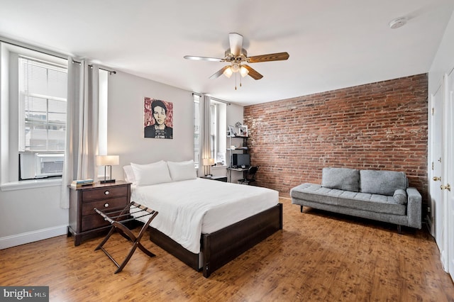 bedroom with ceiling fan, light hardwood / wood-style flooring, and brick wall