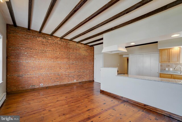 unfurnished living room featuring sink, beam ceiling, hardwood / wood-style floors, and brick wall