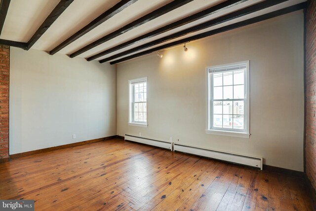 empty room featuring hardwood / wood-style flooring, beam ceiling, a baseboard radiator, and brick wall