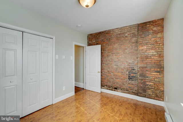 unfurnished bedroom with brick wall, a closet, a baseboard heating unit, and wood-type flooring