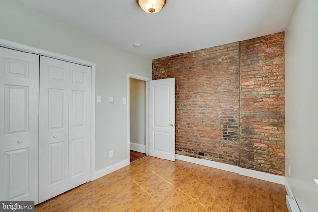 unfurnished bedroom with baseboards, brick wall, baseboard heating, light wood-type flooring, and a closet