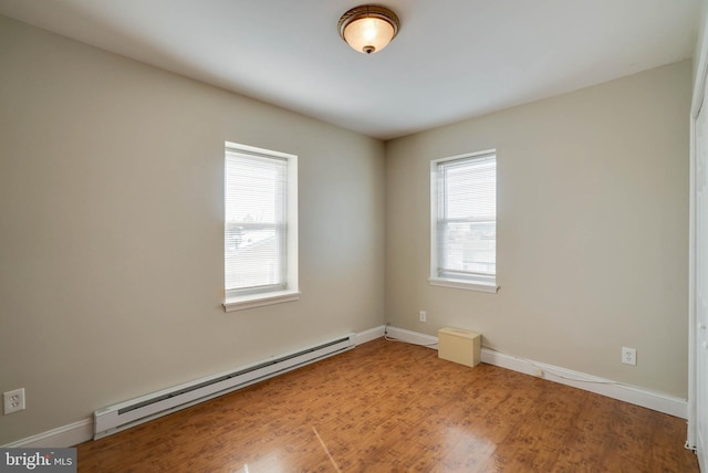 spare room with a baseboard heating unit, wood finished floors, and baseboards