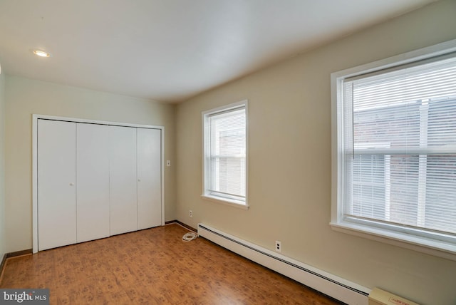 unfurnished bedroom with a baseboard radiator, a closet, a baseboard heating unit, light wood-style floors, and baseboards