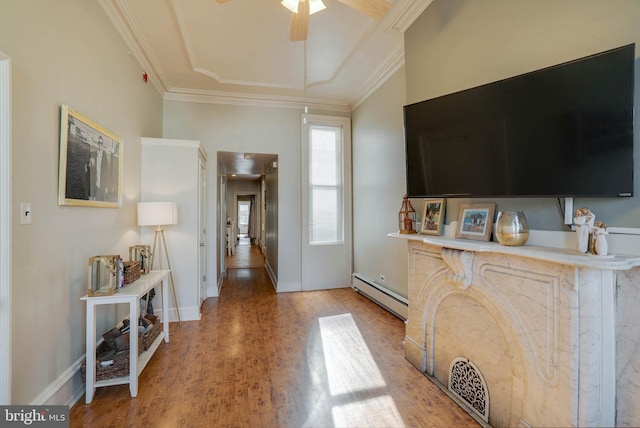 foyer entrance with a baseboard heating unit, a ceiling fan, ornamental molding, and wood finished floors