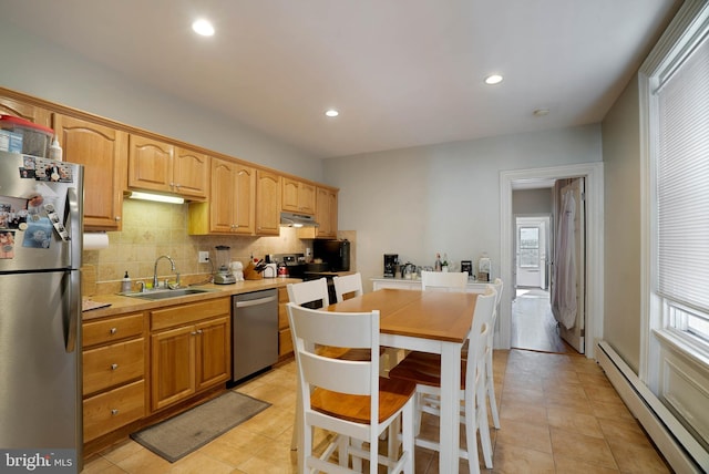 kitchen with a sink, light countertops, appliances with stainless steel finishes, baseboard heating, and backsplash