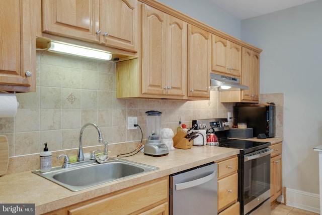 kitchen with appliances with stainless steel finishes, light countertops, a sink, and under cabinet range hood