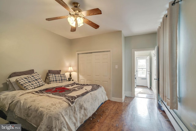 bedroom featuring dark wood-style floors, a baseboard radiator, a closet, a ceiling fan, and baseboards