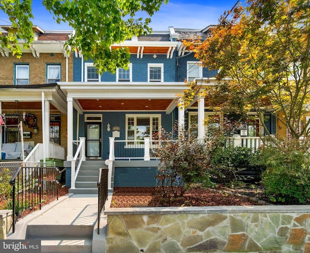 view of property featuring covered porch, mansard roof, and brick siding