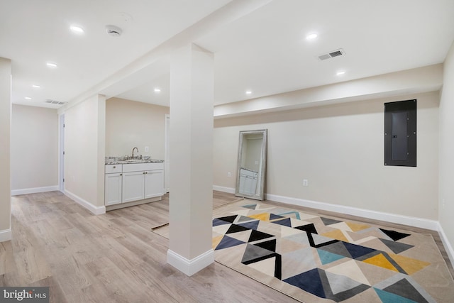 basement with light wood-type flooring, sink, and electric panel