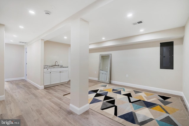 finished basement with light wood-style floors, electric panel, visible vents, and a sink