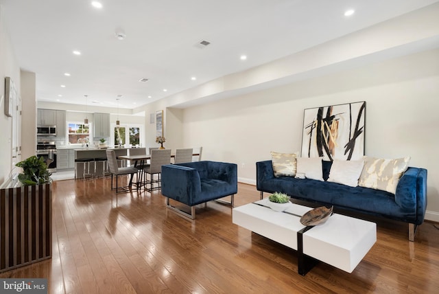 living room featuring light wood-style floors, baseboards, visible vents, and recessed lighting