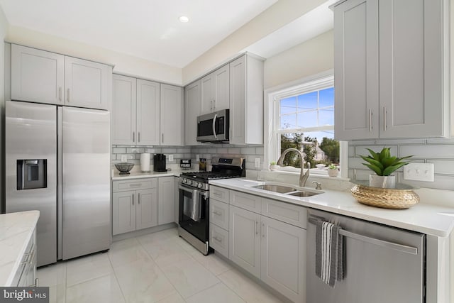 kitchen featuring light stone counters, tasteful backsplash, gray cabinetry, appliances with stainless steel finishes, and a sink