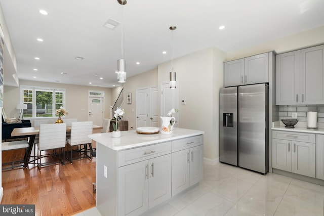 kitchen featuring light hardwood / wood-style flooring, gray cabinetry, stainless steel fridge with ice dispenser, a center island, and hanging light fixtures