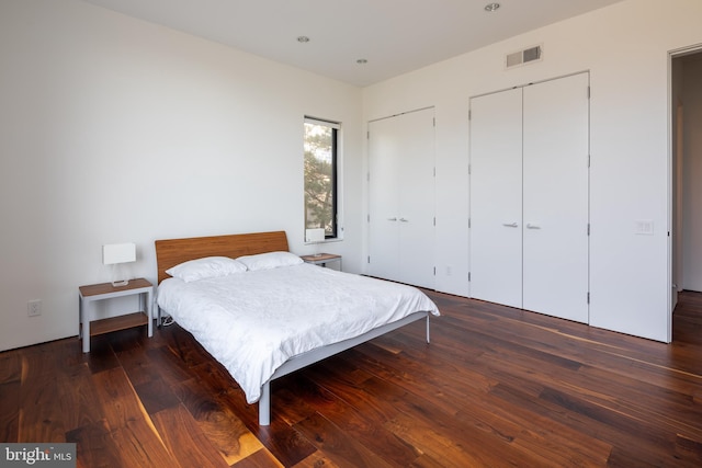 bedroom featuring wood finished floors, visible vents, and two closets