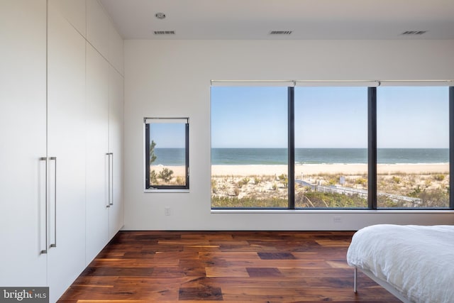 bedroom with a view of the beach, a water view, wood finished floors, and visible vents