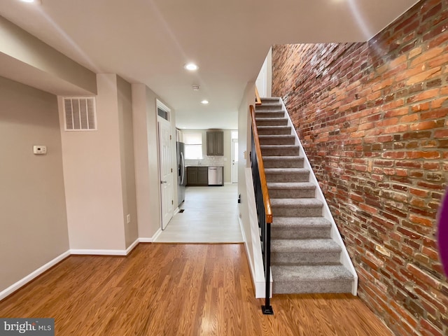 stairs with wood-type flooring and brick wall