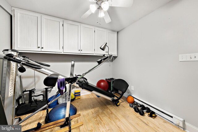 workout area with ceiling fan, a baseboard heating unit, and light wood-type flooring