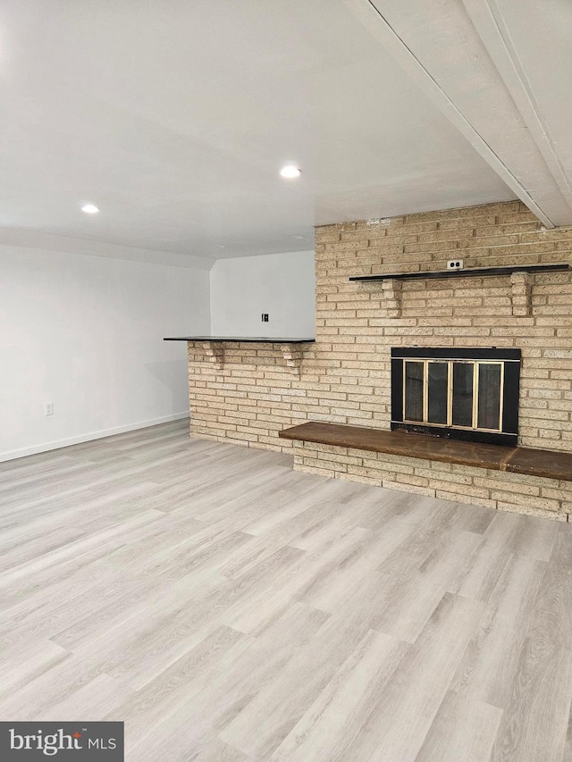 unfurnished living room featuring a fireplace, brick wall, and wood-type flooring