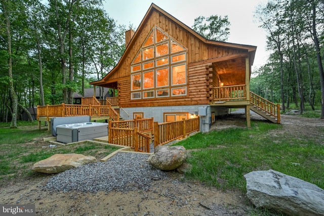 rear view of house with stairs, log exterior, a chimney, and a hot tub