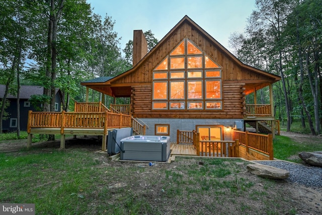 rear view of property featuring a hot tub, a lawn, log exterior, a chimney, and a deck