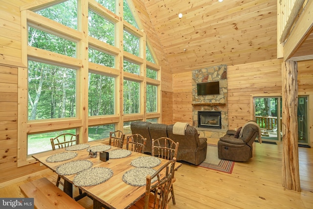 dining room with high vaulted ceiling, wooden ceiling, light wood-style flooring, wooden walls, and a fireplace