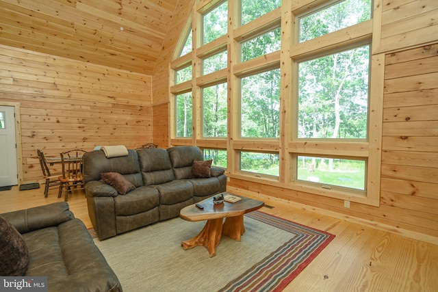 living area with high vaulted ceiling, plenty of natural light, wood ceiling, and wooden walls